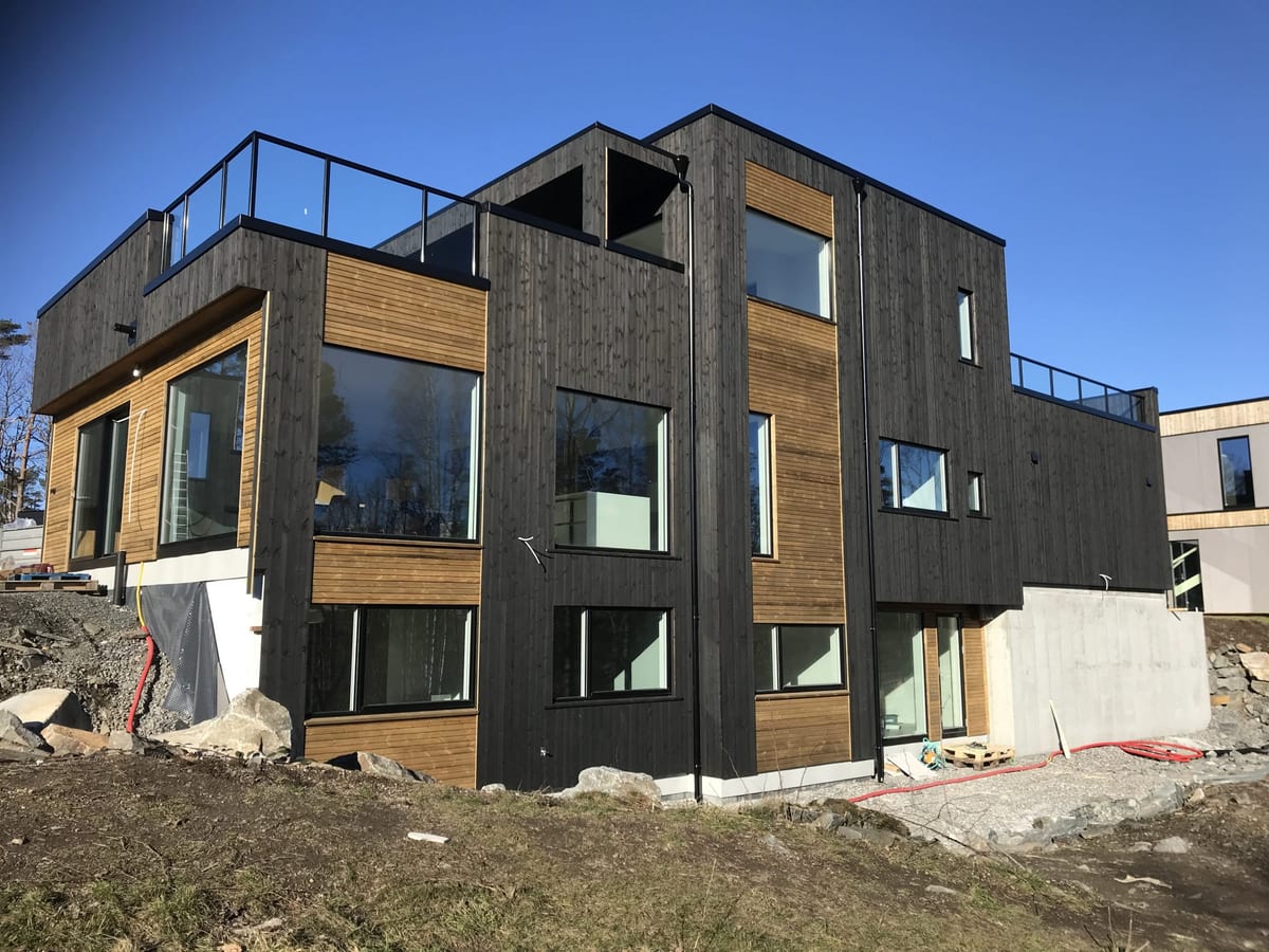 Nytt, moderne hus i tre etasjer med sort kledning og store vinduer, bygget av Byggfirma Martin Unhjem